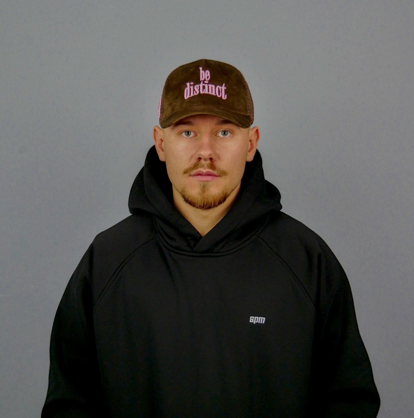 KELIX Velours Cap in Braun mit pinkem 'be distinct' Stick โ Seitenansicht und Frontansicht einer Person, die die Kappe trรคgt, dazu das Logo auf dem schwarzen Hoodie sichtbar.