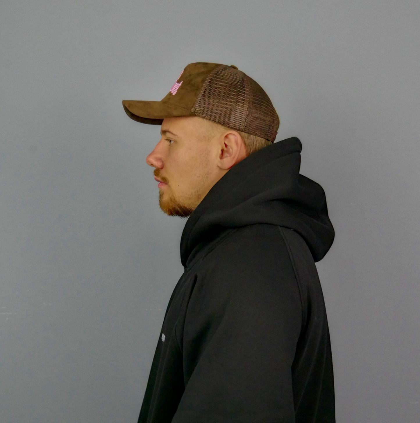KELIX Velours Cap in Braun mit pinkem 'be distinct' Stick โ Seitenansicht und Frontansicht einer Person, die die Kappe trรคgt, dazu das Logo auf dem schwarzen Hoodie sichtbar.โ