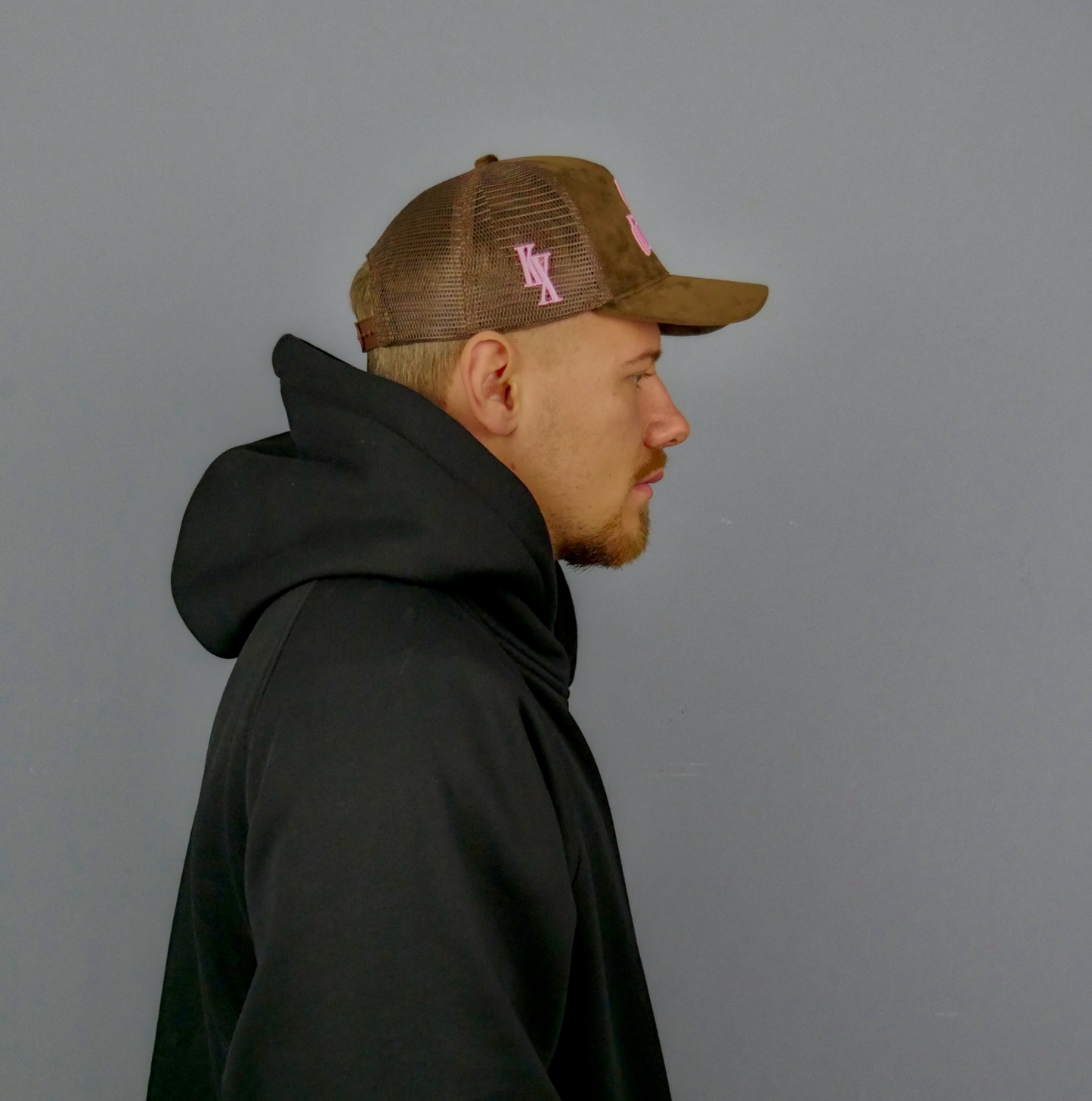 KELIX Velours Cap in Braun mit pinkem 'be distinct' Stick โ Seitenansicht und Frontansicht einer Person, die die Kappe trรคgt, dazu das Logo auf dem schwarzen Hoodie sichtbar.
