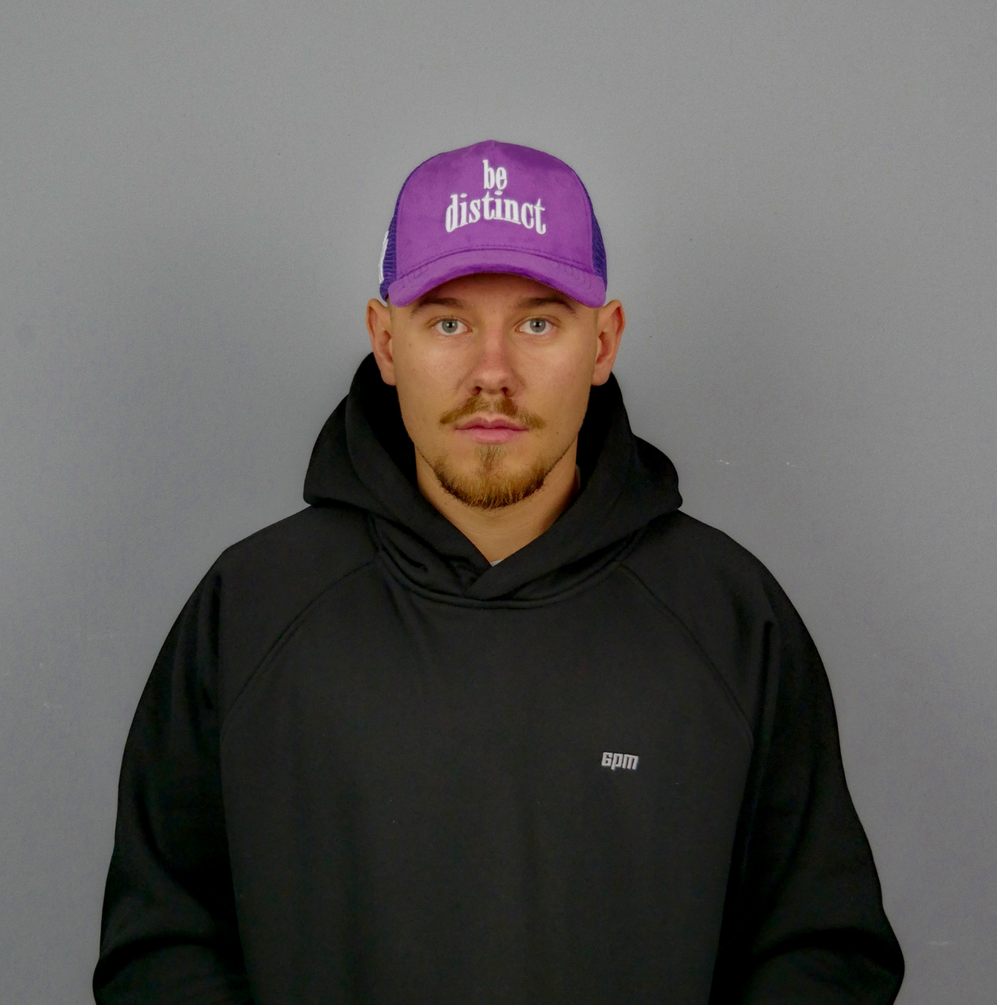 KELIX Velours Cap in Lila mit weiรem 'be distinct' Stick โ Frontansicht einer Person, die die Kappe trรคgt, zusammen mit einer Seitenansicht der Kappe und einer weiteren Person im schwarzen Hoodie mit lila Kappe.