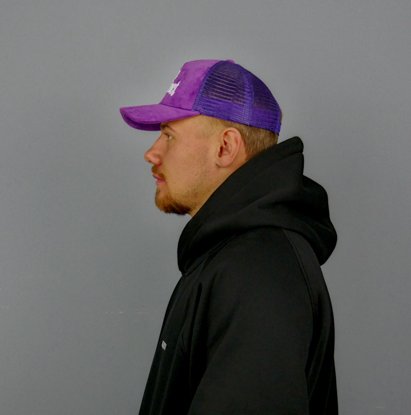 KELIX Velours Cap in Lila mit weiรem 'be distinct' Stick โ Frontansicht einer Person, die die Kappe trรคgt, zusammen mit einer Seitenansicht der Kappe und einer weiteren Person im schwarzen Hoodie mit lila Kappe.