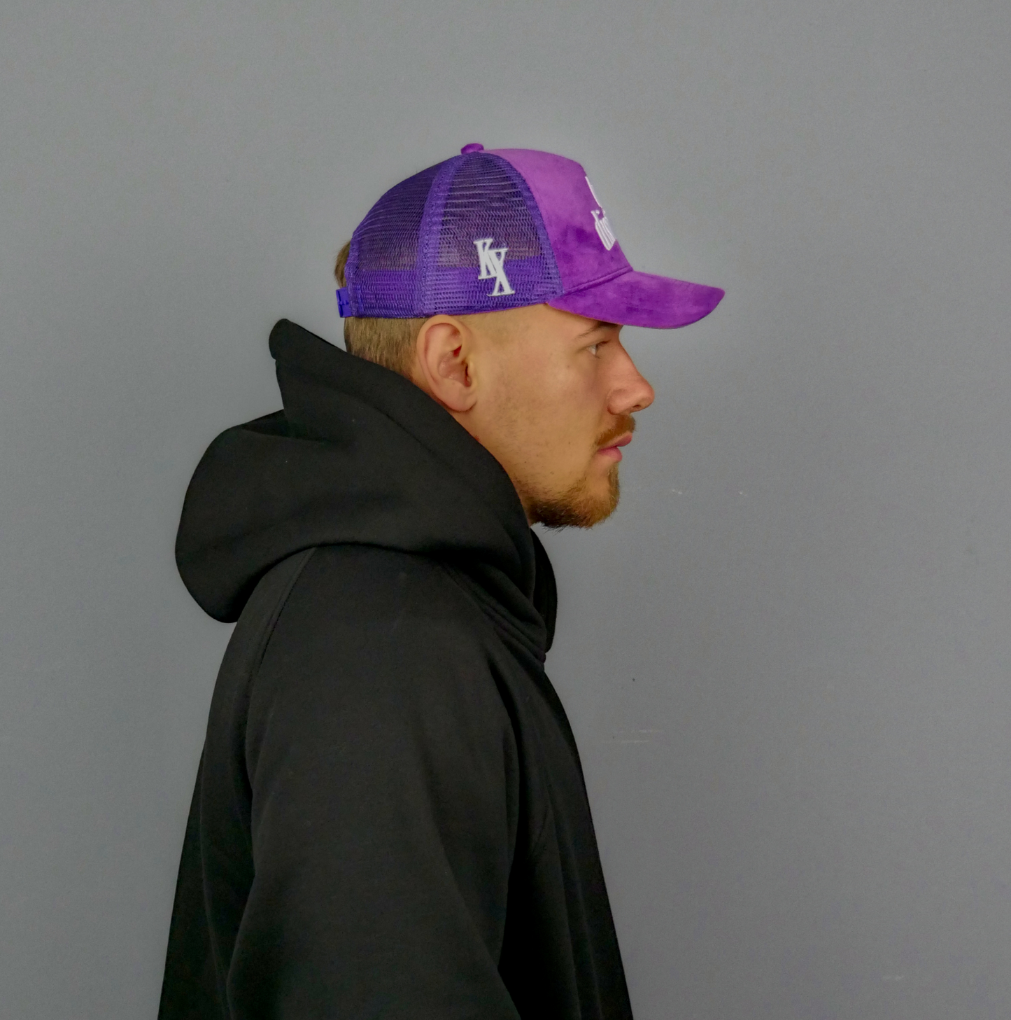 KELIX Velours Cap in Lila mit weiรem 'be distinct' Stick โ Frontansicht einer Person, die die Kappe trรคgt, zusammen mit einer Seitenansicht der Kappe und einer weiteren Person im schwarzen Hoodie mit lila Kappe