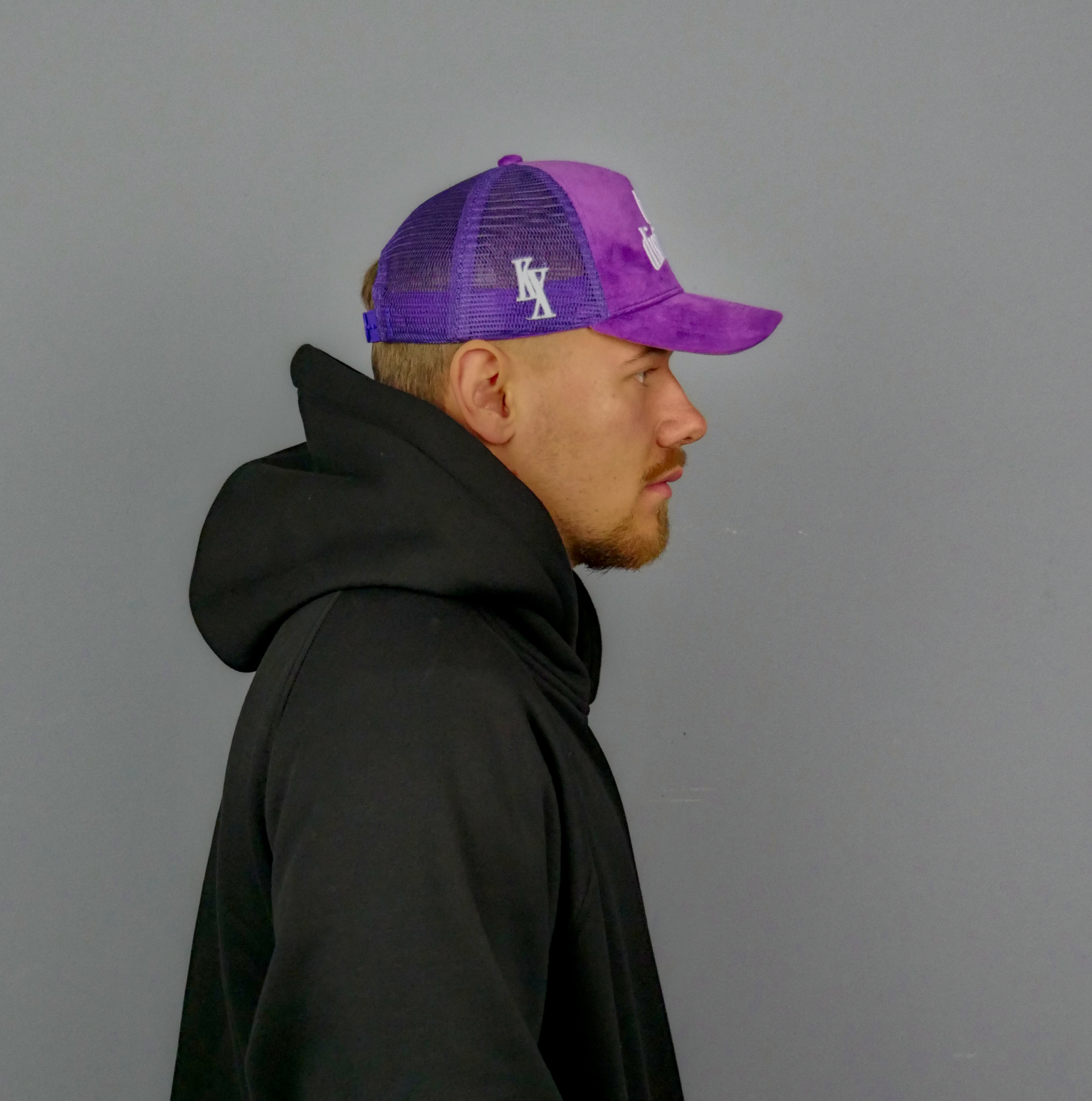 KELIX Velours Cap in Lila mit weißem 'be distinct' Stick – Frontansicht einer Person, die die Kappe trägt, zusammen mit einer Seitenansicht der Kappe und einer weiteren Person im schwarzen Hoodie mit lila Kappe